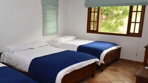 A room with two beds, a television, and a window with a view of greenery. - Hotel Campestre Bachue (Villa de Leyva)