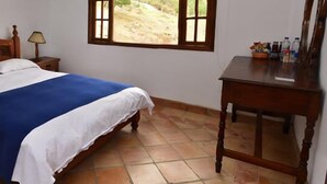 A bedroom with a wooden bed, a nightstand, a bedside lamp, a window with a view, and a wooden dresser. - Hotel Campestre Bachue (Villa de Leyva)