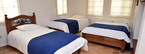Una habitación con tres camas individuales, cada una con cabecero de madera y ropa de cama blanca.