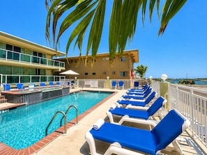 A pool area with lounge chairs and a building in the background. - Crystal Beach Motor Inn (Wildwood Crest)