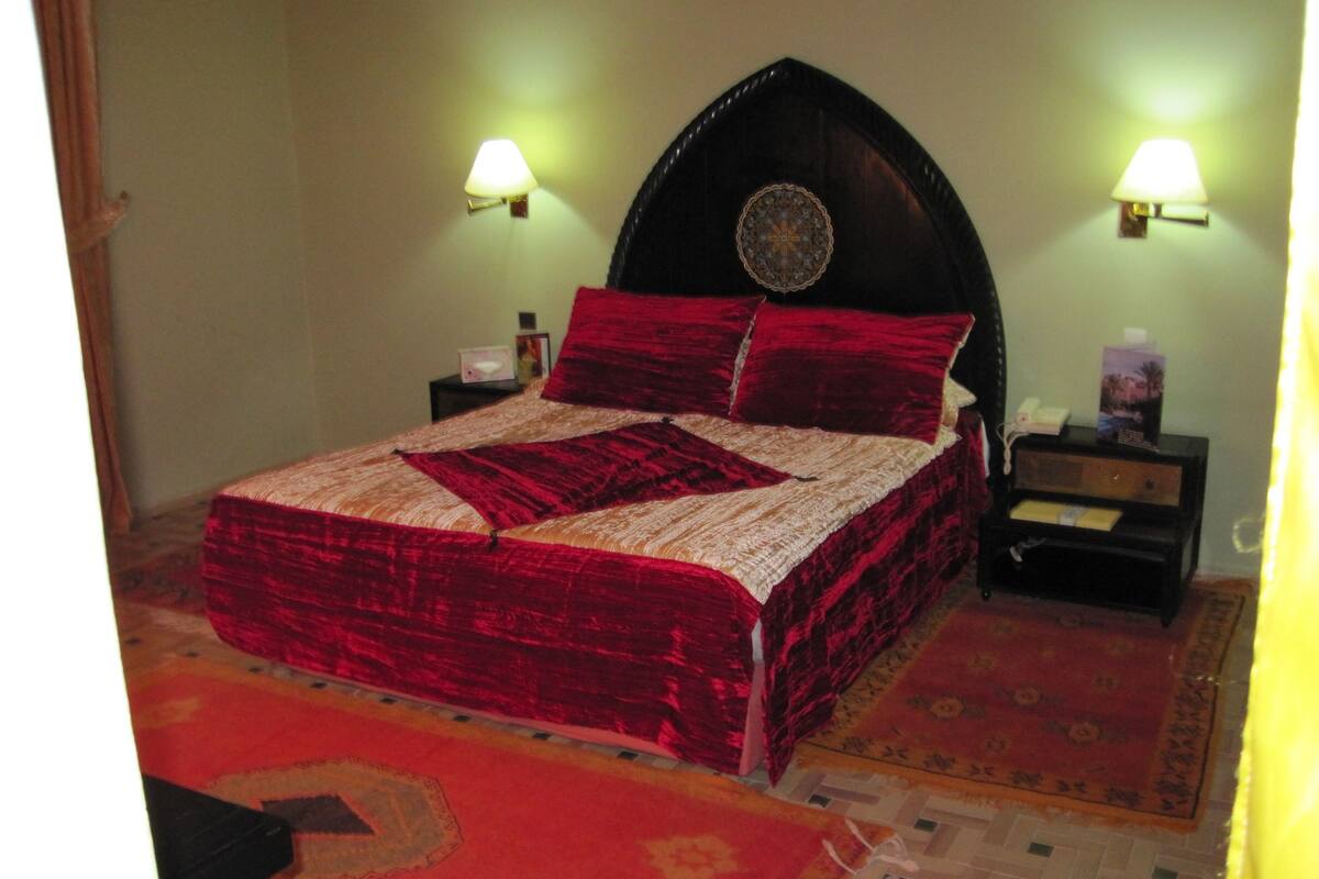 A bed with a red and beige bedspread, two nightstands with lamps, and a patterned rug on the floor.