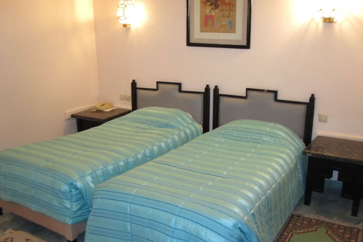 A room with two single beds, a nightstand with a phone, and a framed picture on the wall.