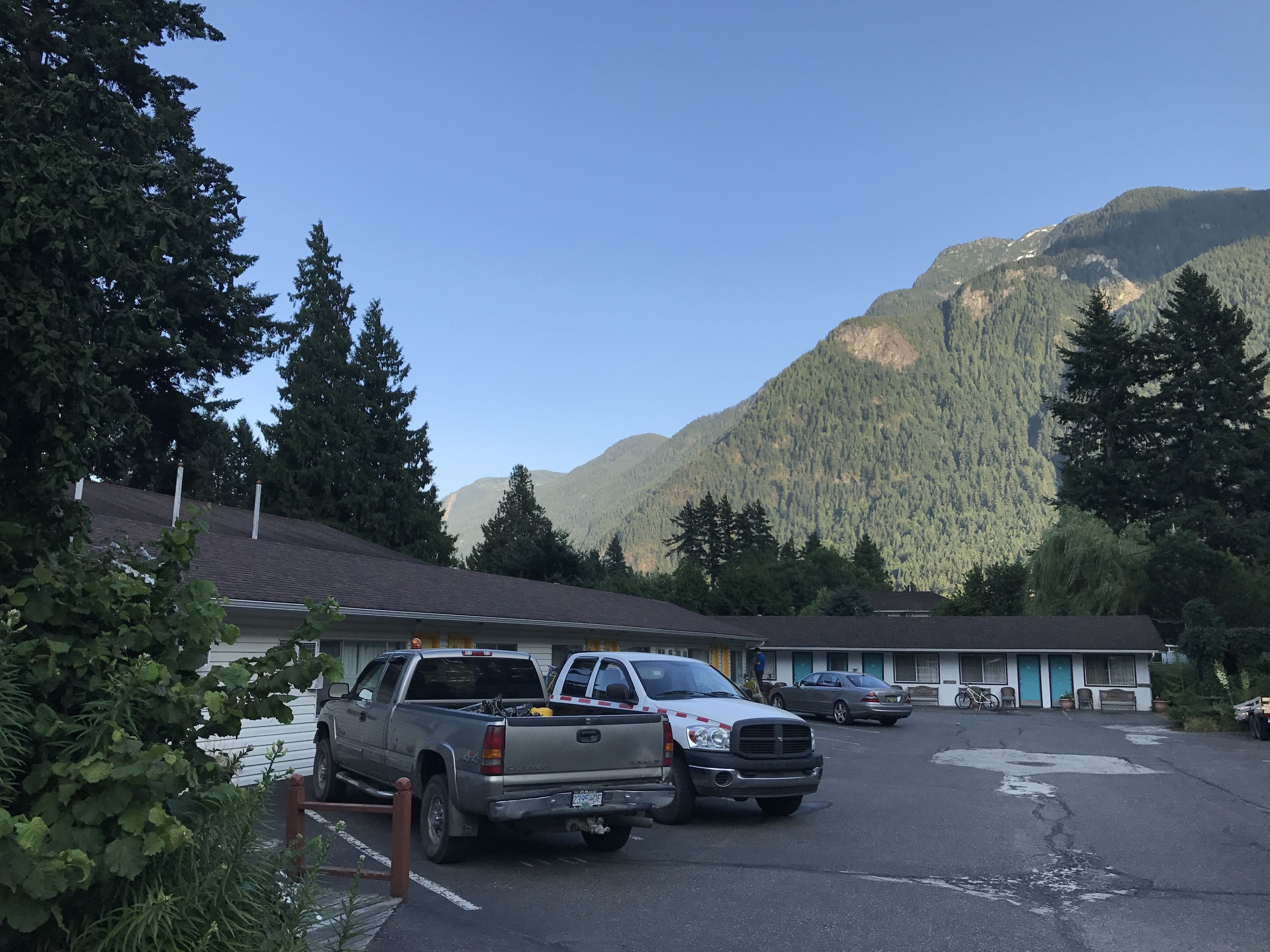 A motel with a parking lot, a mountain backdrop, and a building with a flat roof.