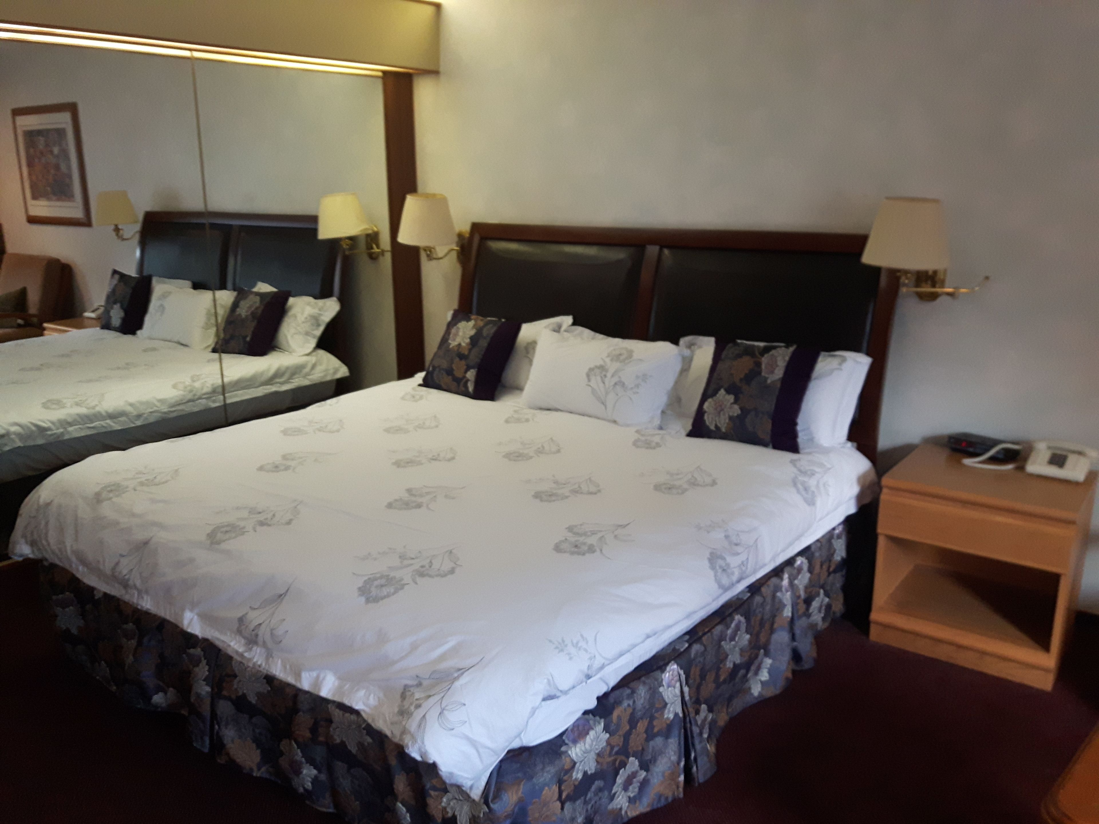 Une chambre d’hôtel avec deux lits, chacun agrémenté de draps à motifs floraux, de lampes de chevet et d’une table de nuit en bois avec un téléphone.