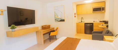 Habitación de hotel con cama, escritorio, silla, televisor, cocina y microondas.