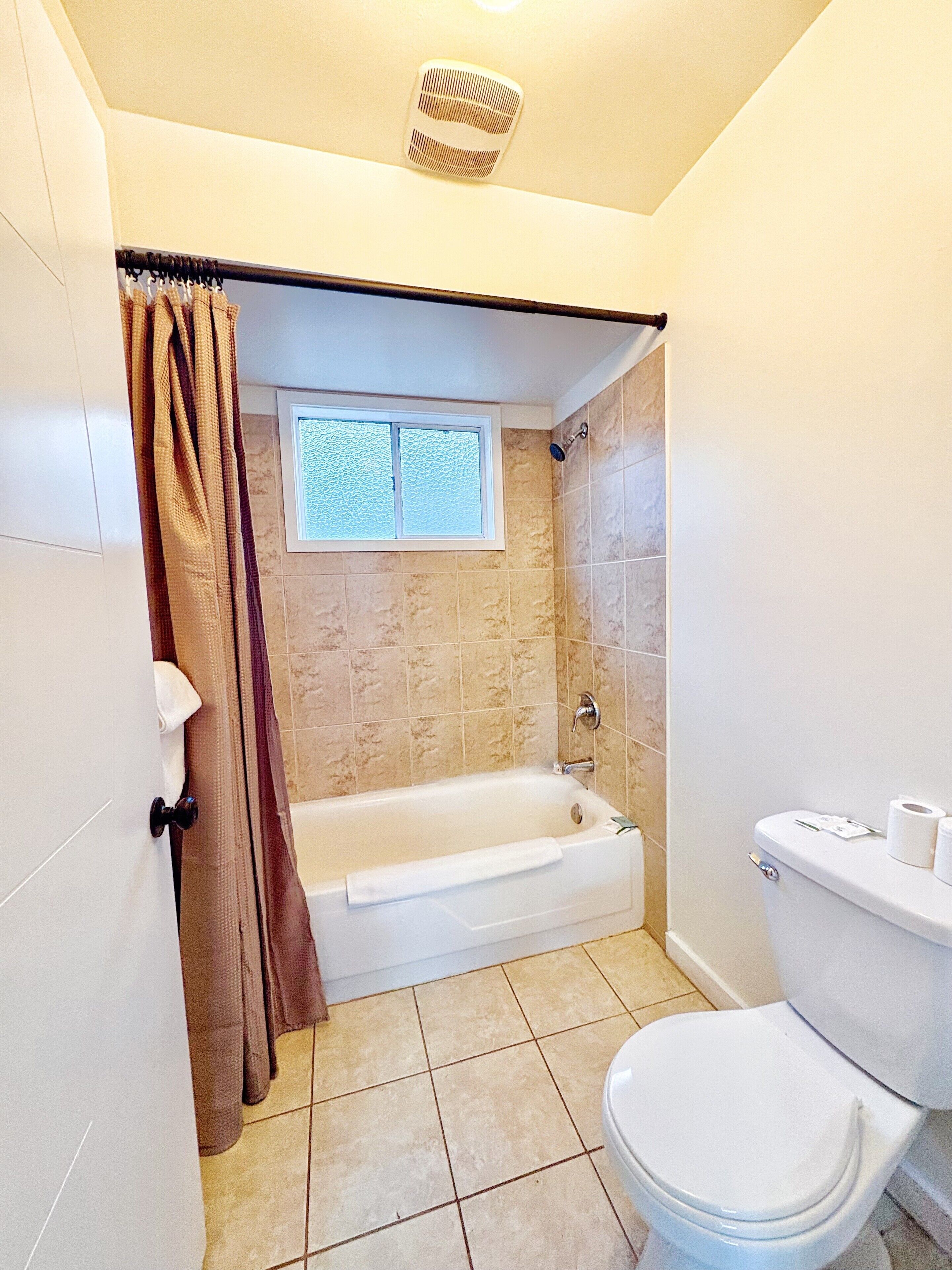 A bathroom with a bathtub, toilet, and a window above the shower.