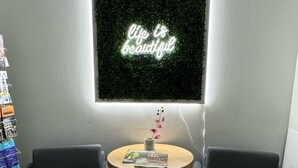 A room with two dark armchairs, a small round table with magazines, and a neon sign on the wall. - Inn Towne Motel (Hope)