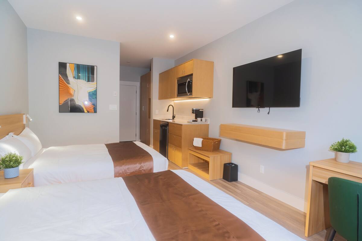 Une chambre d’hôtel avec deux lits, une kitchenette, un téléviseur à écran plat et un bureau avec une chaise.