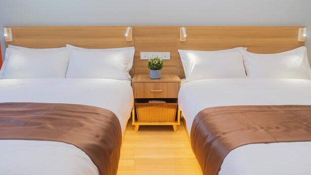 A double bed room with a wooden headboard, two bedside tables with lamps, a small potted plant, and a wicker basket. - Inn Towne Motel (Hope)