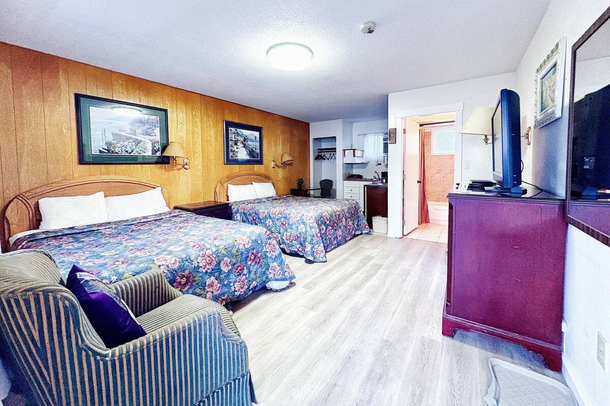 Une chambre d’hôtel avec deux lits, un mur recouvert de panneaux en bois, un bureau avec un ordinateur et une télévision.
