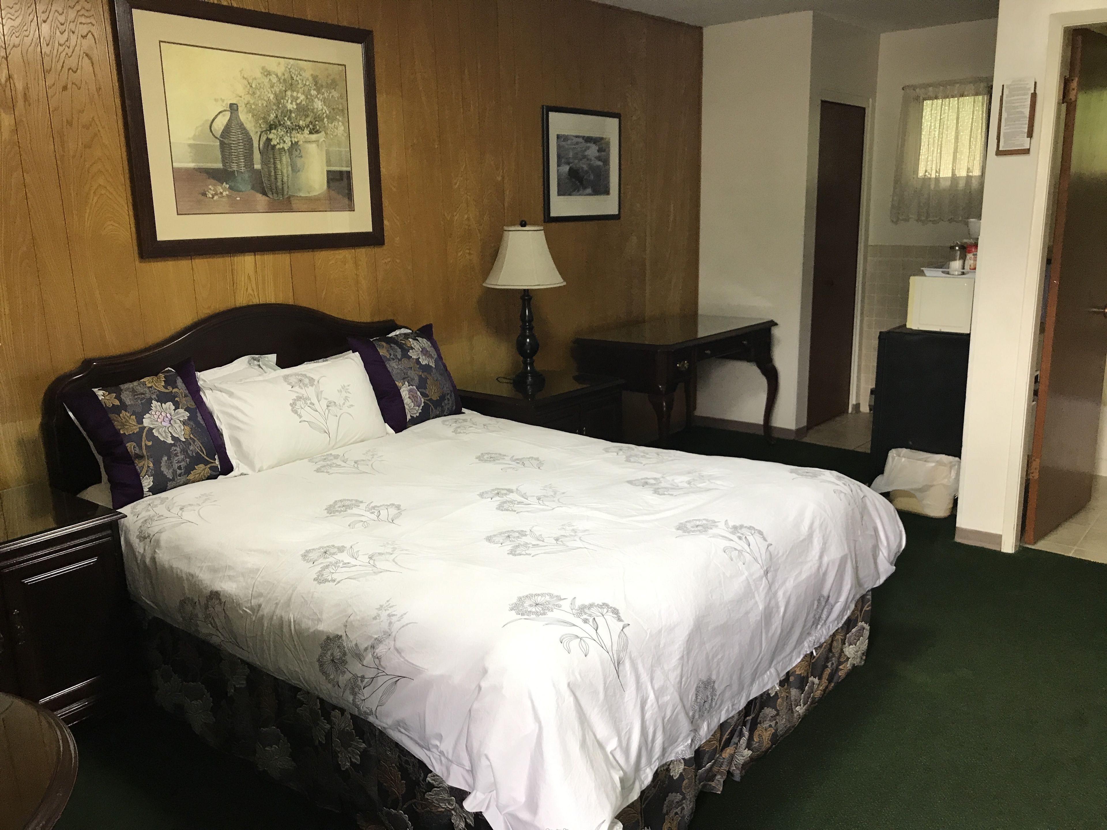 A hotel room with a large bed, a bedside table, a lamp, and a framed picture on the wall.