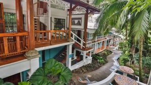 A multi-story building with wooden balconies, a covered walkway, and lush tropical vegetation.