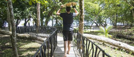 A person walking on a wooden bridge with metal railings, surrounded by trees and greenery.