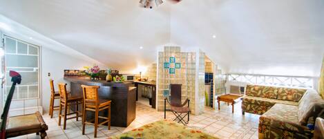 A spacious living area with a high ceiling, a ceiling fan, a dining area with chairs, a sofa, and a small table.