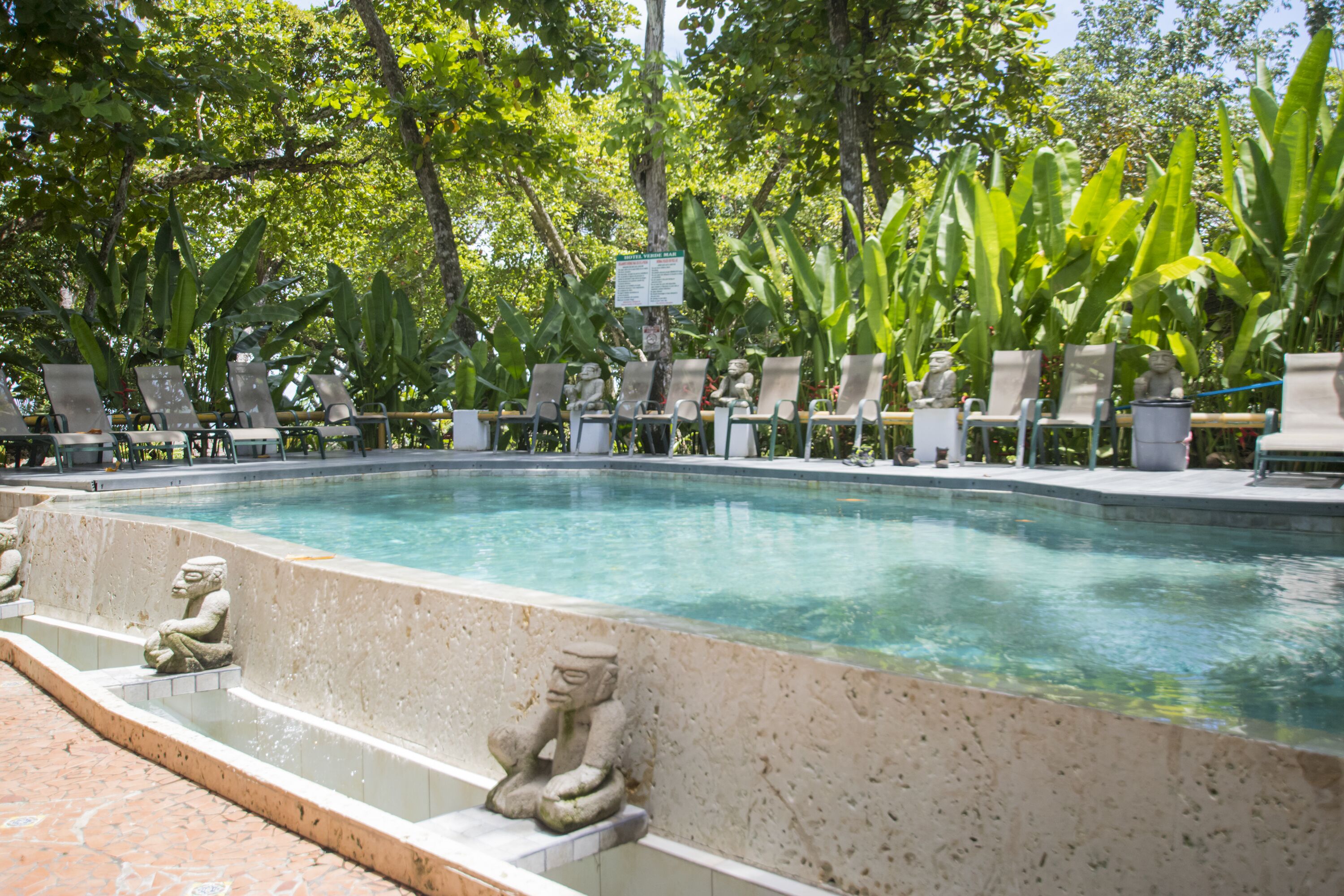 A pool with stone statues and lounge chairs.