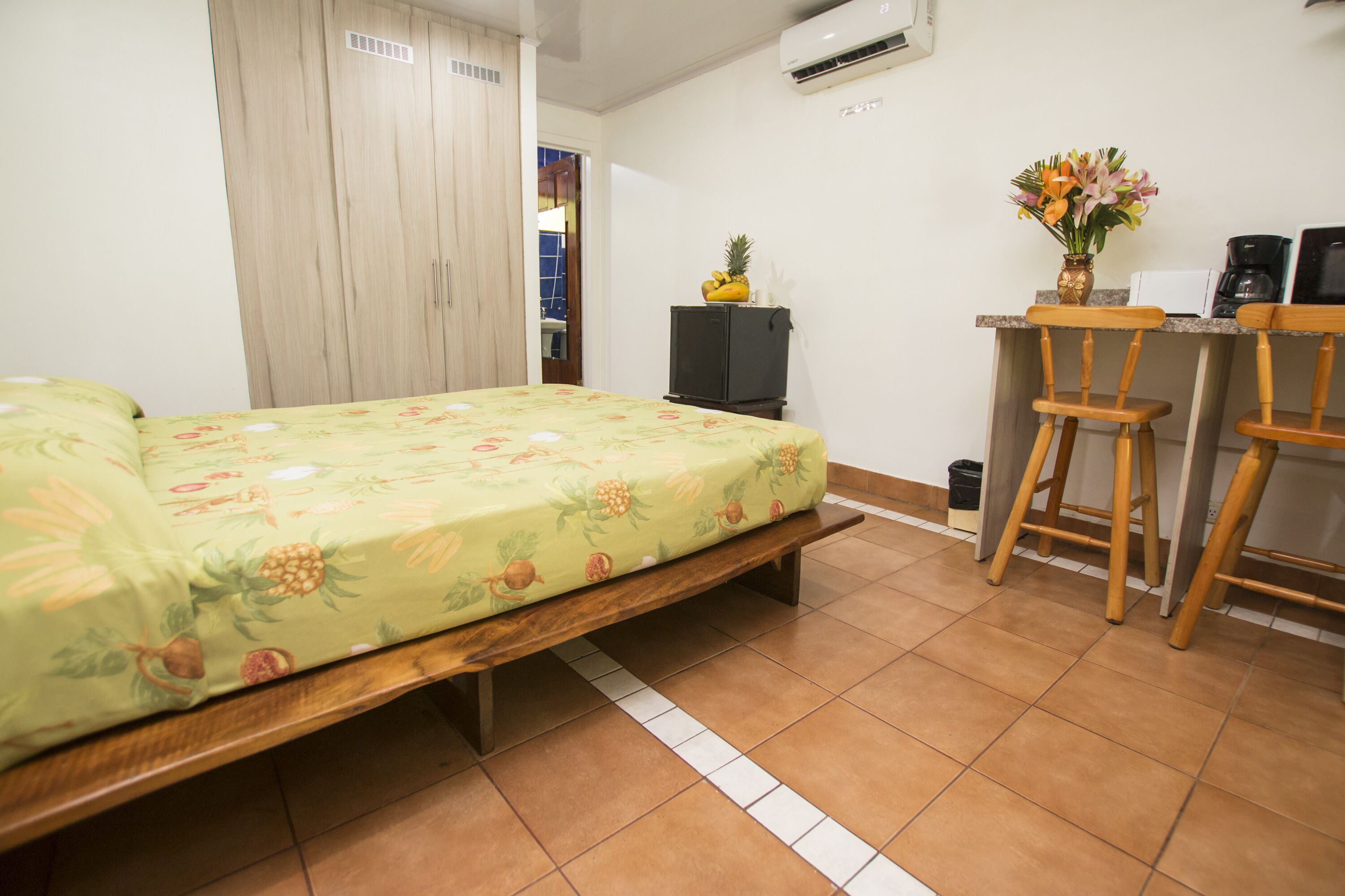 Een slaapkamer met een bed, een bureau met stoelen en een kleine koelkast.