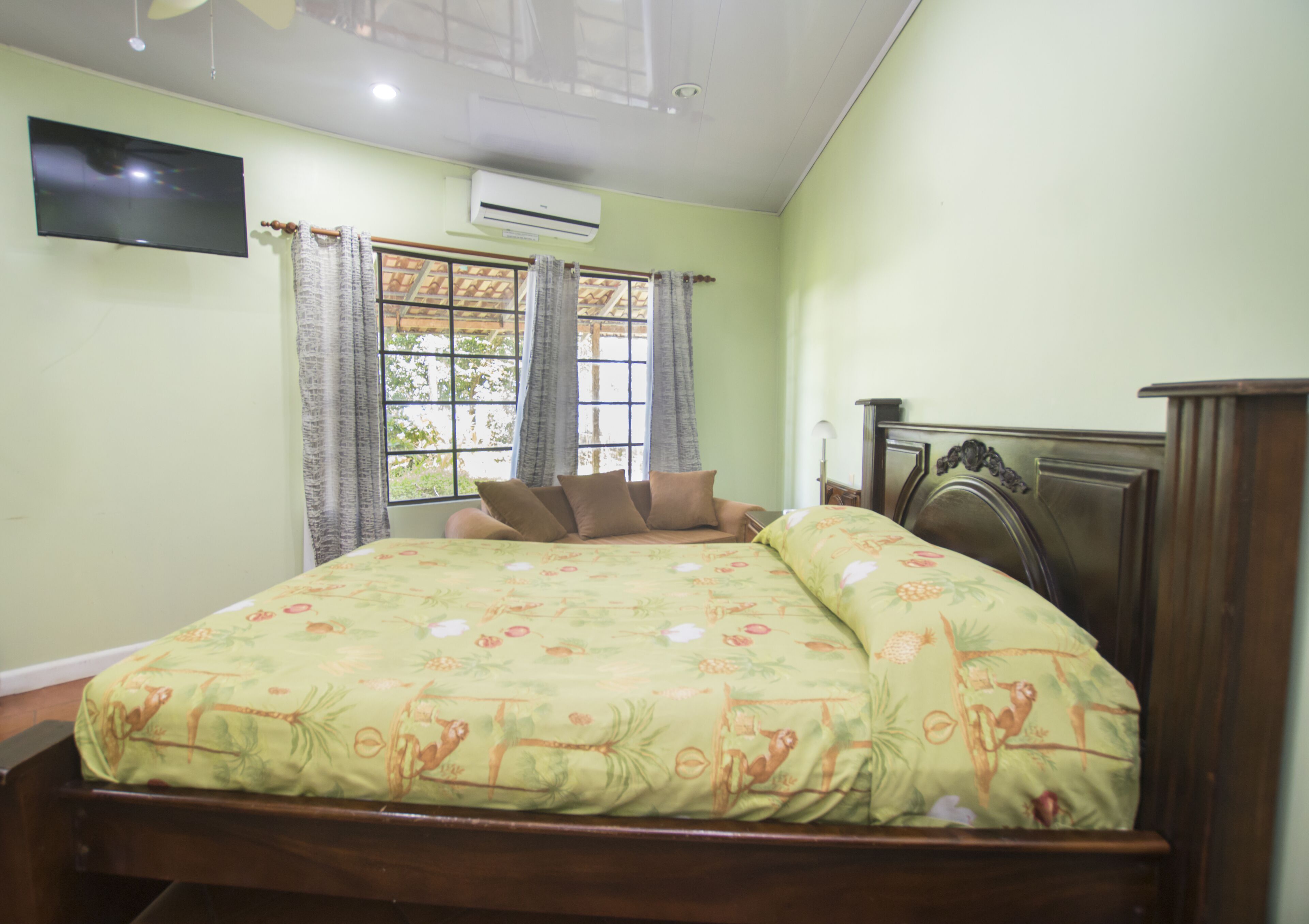 A bedroom with a bed, a flat-screen TV, an air conditioner, and a window with curtains.