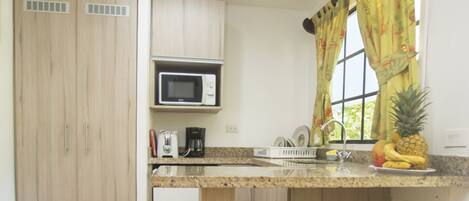 A compact kitchen with a microwave, sink, and bar stools.