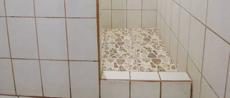 A small, tiled bathroom with a shower area, a tiled floor, and a white towel on the floor.