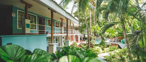 Un hotel con struttura su due piani, una zona esterna coperta e una piscina immersa nel verde.
