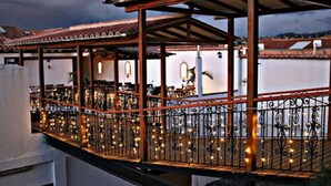 A covered outdoor area with a railing, string lights, and a view of the cityscape in the background. - Hospedería Villa de Los Saenz (Villa de Leyva)