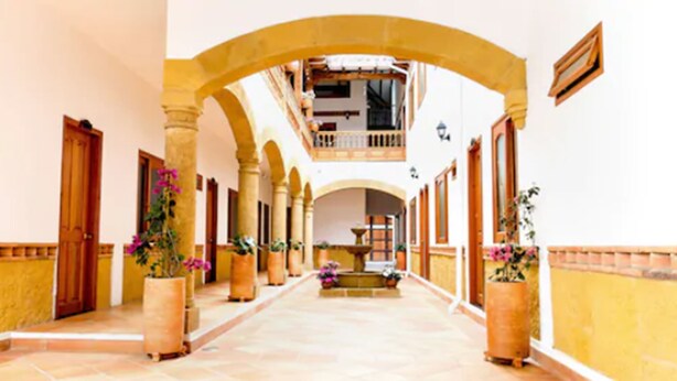 A corridor with arches, potted plants, and a fountain. - Hospedería Villa de Los Saenz (Villa de Leyva)
