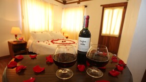 A room with a bed, a table with two glasses of red wine, a bottle of wine, and rose petals. - Hospedería Villa de Los Saenz (Villa de Leyva)