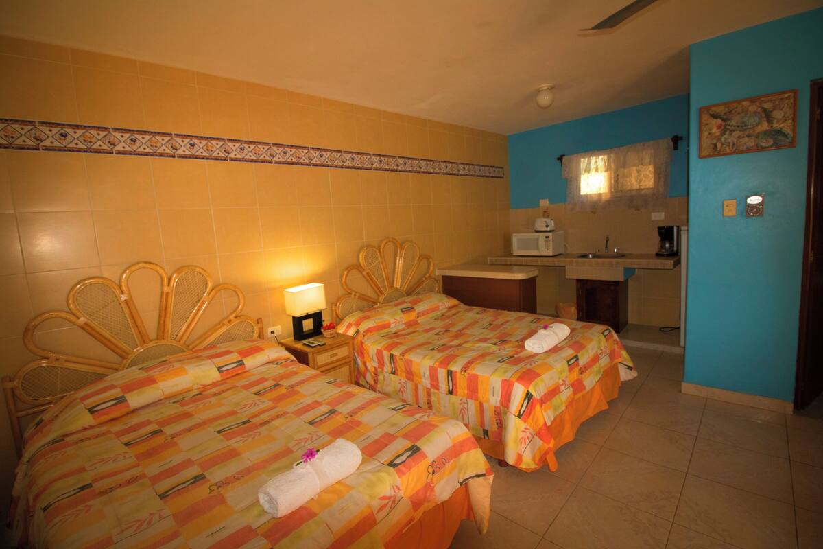 A hotel room with two beds, a small kitchenette, and a bathroom.