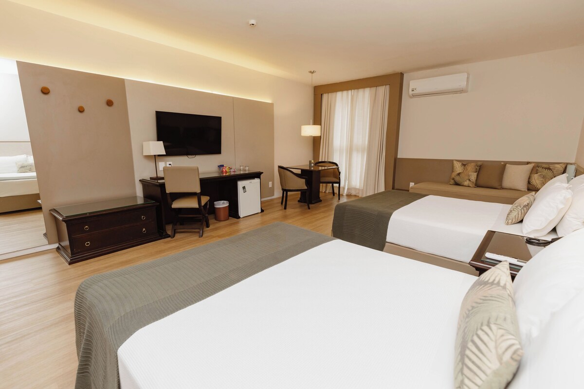 Habitación de hotel con dos camas, un escritorio, un televisor y una ventana con cortinas.