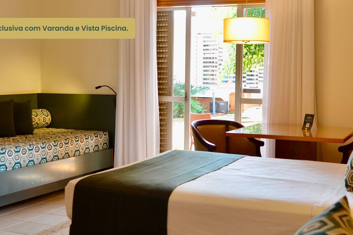 A hotel room with two beds, a desk, and a chair. There is a window with blinds, and a lamp on the desk.