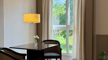 A modern dining area with a wooden table and chairs, a hanging lamp, and a view of a garden through a large window with curtains.
