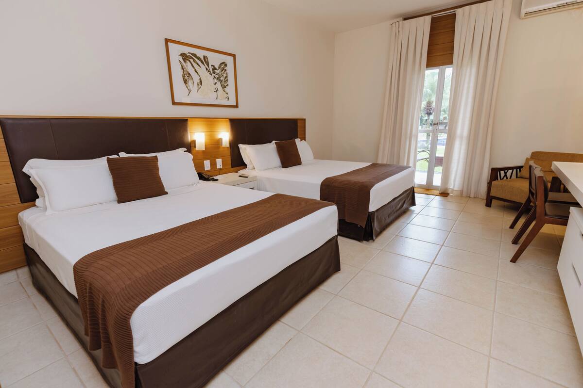A hotel room with two beds, a desk, a chair, and a window with curtains.