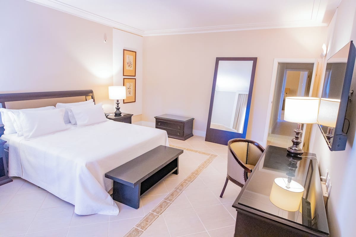 A hotel room with a large bed, bedside table, lamp, chair, and a mirror.
