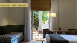 Habitación de hotel con cama, escritorio, sillón y sofá. Se ve una piscina y vegetación al exterior.