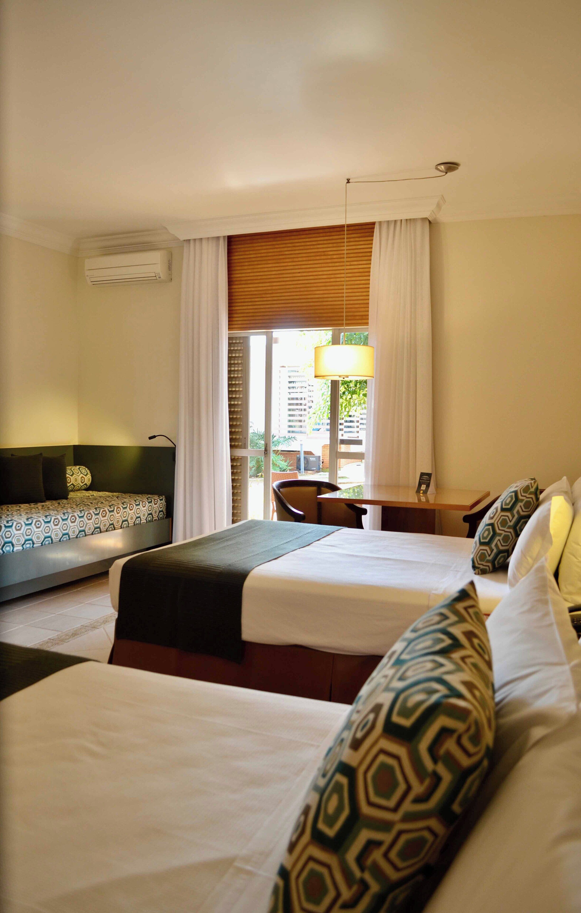 A hotel room with two beds, a desk, a chair, and a window with curtains.