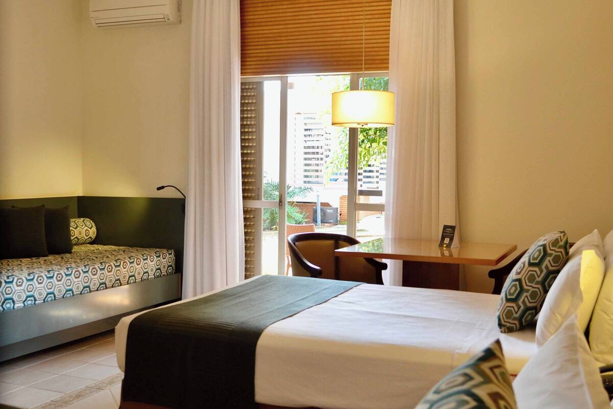 A hotel room with two beds, a desk, a chair, and a window with curtains.