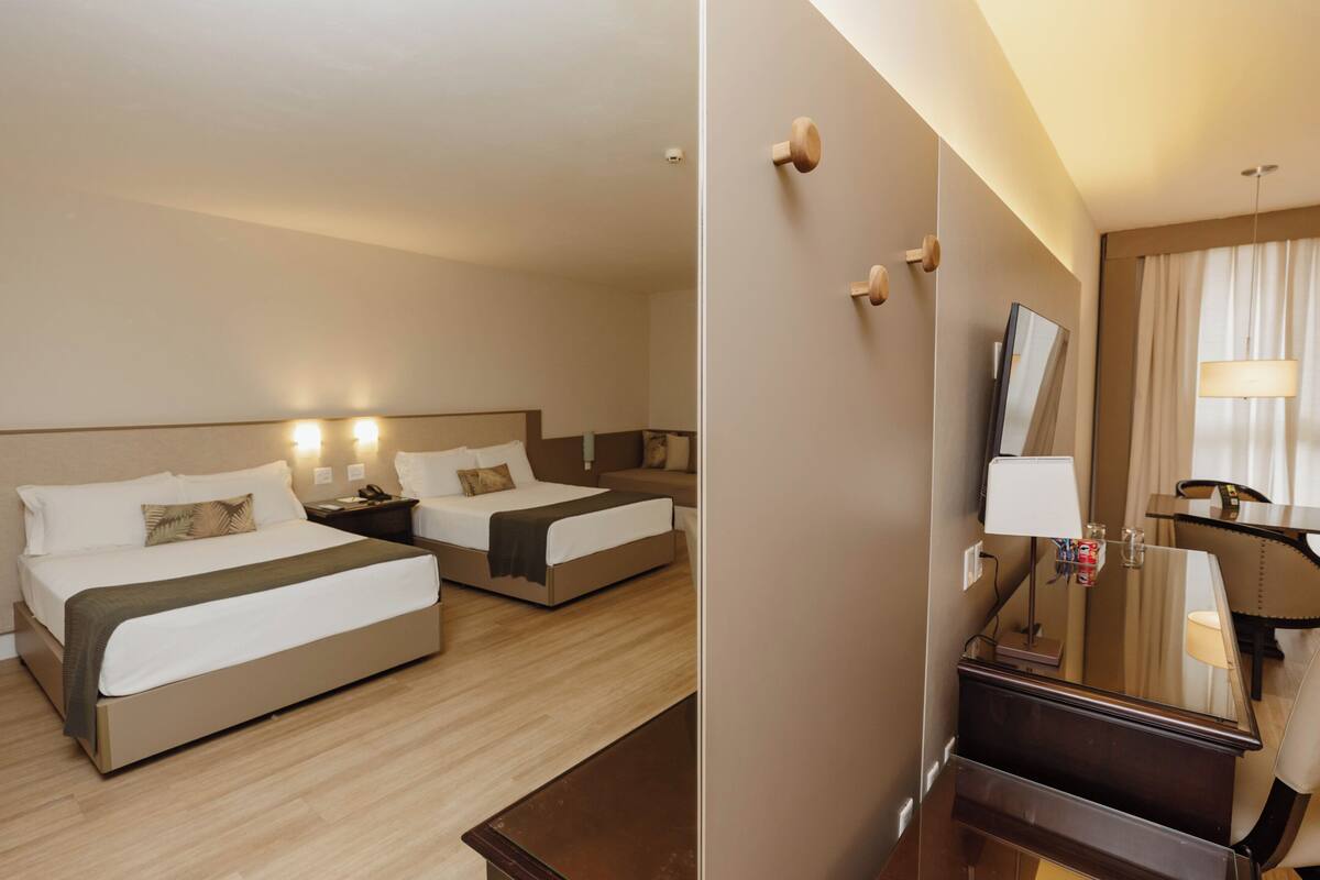 Ein Hotelzimmer mit zwei Betten, einem Schreibtisch, einem Stuhl, einem Spiegel und einer Lampe.