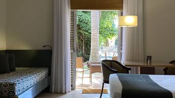 Ein Hotelzimmer mit Bett, Schreibtisch, Stuhl und einer Couch. Blick auf einen Pool und Grünfläche.