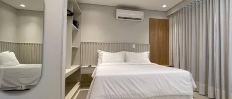 A modern bedroom with a large bed, a bedside table, a mirror, and a built-in air conditioning unit.