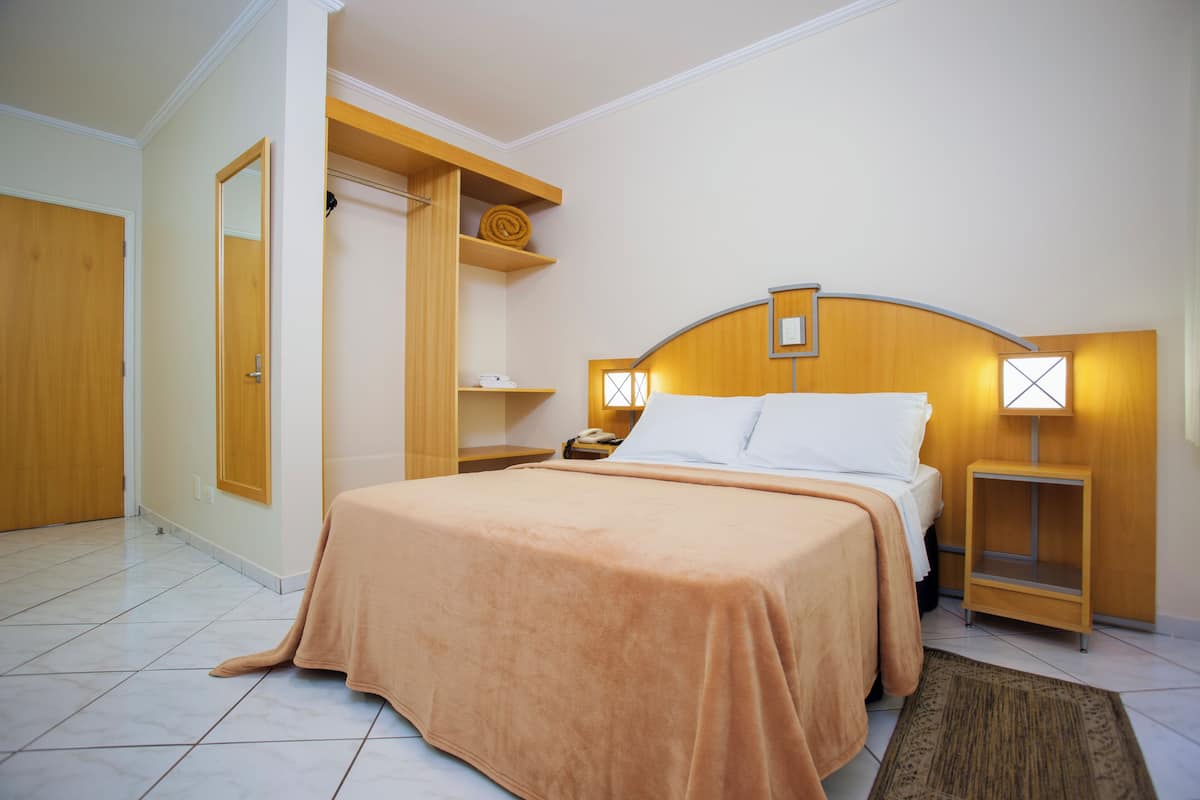 Hotellihuone, jossa on sänky, yöpöydät, puinen vaatekaappi ja peili.