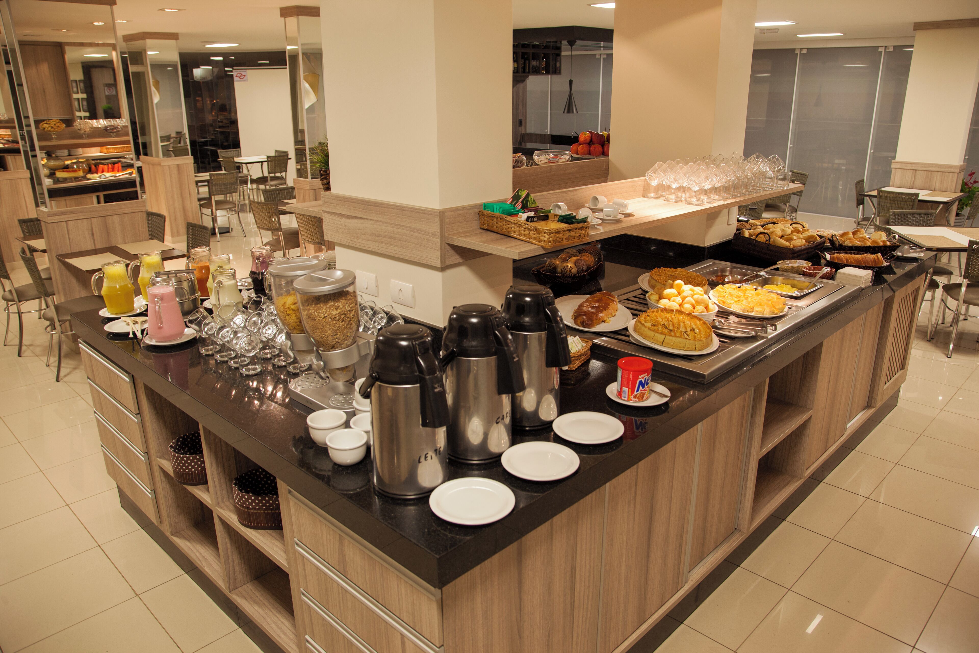 Disposição de buffet com diversos alimentos, máquinas de café e copos.