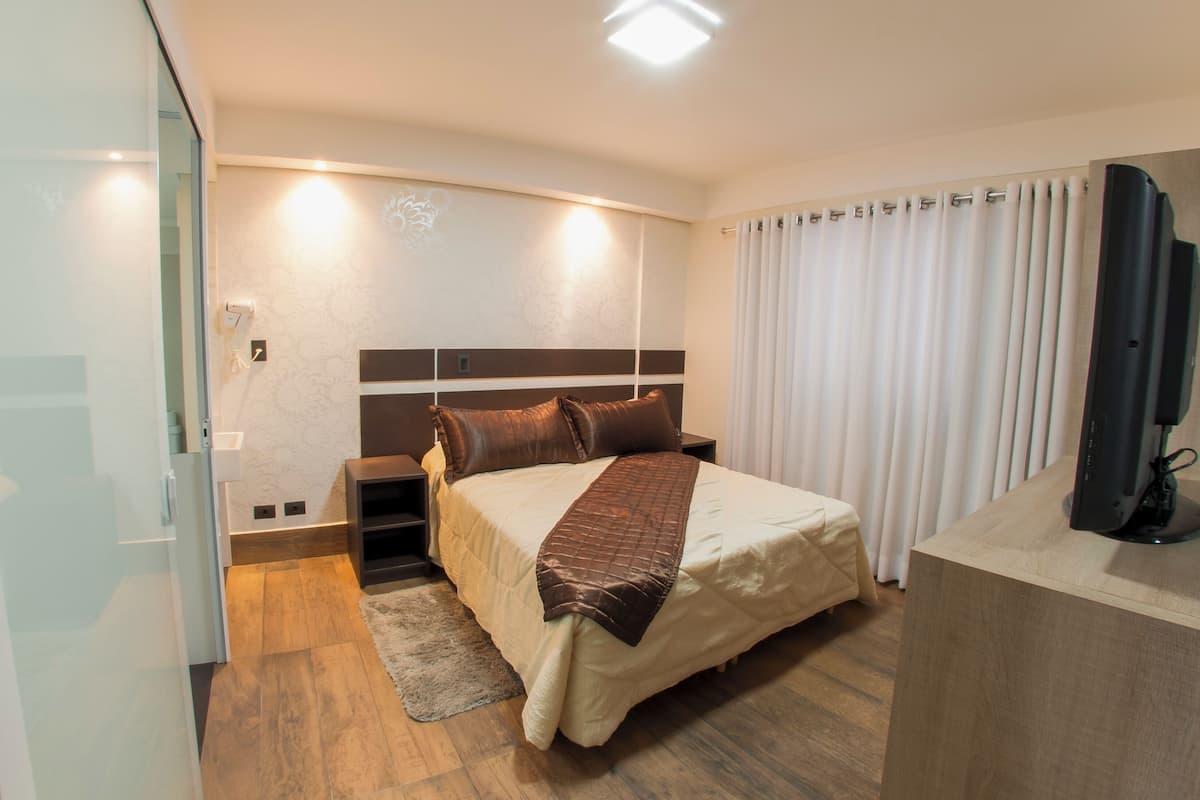 Moderni hotellihuone, jossa on suuri sänky, taulutelevisio ja puulattia.