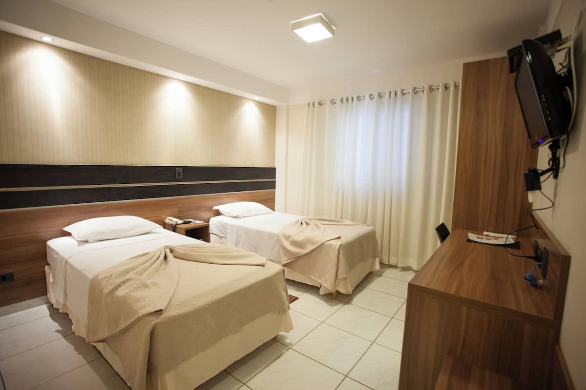 Hotellihuone, jossa on kaksi sänkyä, puinen työpöytä, televisio ja ikkuna, jossa on verhot.