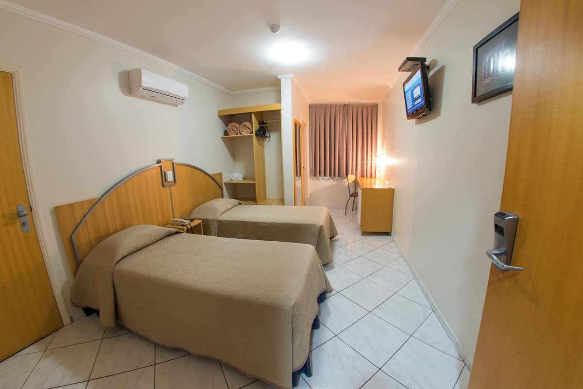 Hotellihuone, jossa on kaksi sänkyä, puinen pääty, yöpöytä, pieni työpöytä, tuoli, televisio ja ilmastointilaite.