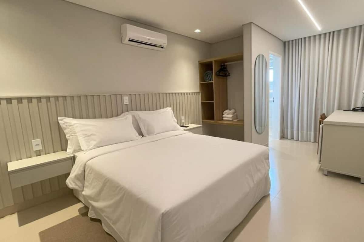 Moderni hotellihuone, jossa on suuri sänky, yöpöytä, vaatekaappi ja työpöytä.