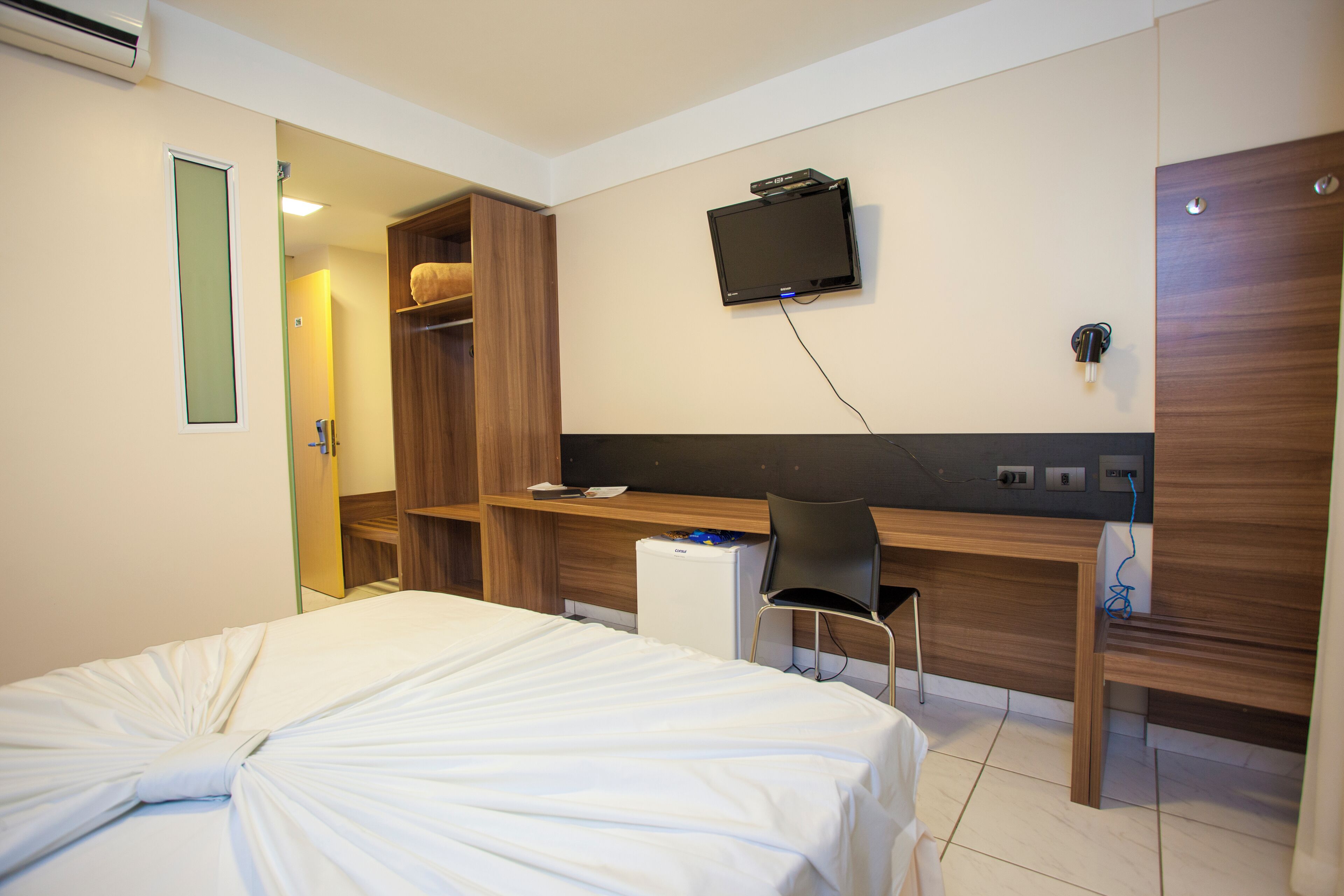 A hotel room with a bed, a desk, a chair, a television, and a wardrobe.