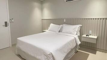 Quarto de hotel moderno com uma cama grande, uma mesinha de cabeceira, um ar condicionado e uma porta com fechadura.