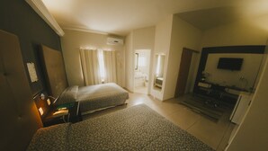 A hotel room with two beds, a small kitchenette, a bathroom, and a TV mounted on the wall. - Villa Verde Hotel (Avare)