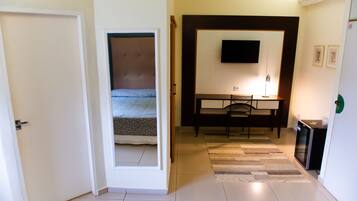 A hotel room with a bed, a desk, a chair, a television, and a small kitchen area.