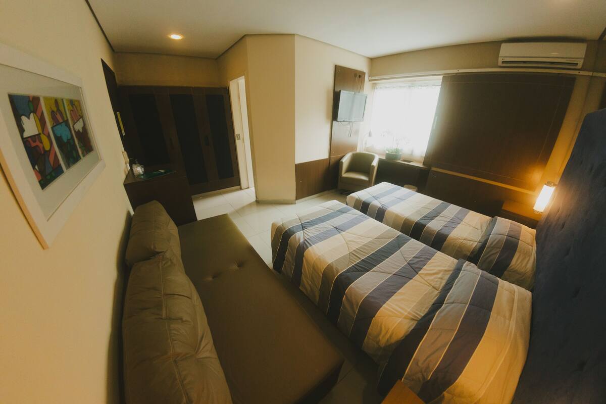 Habitación de hotel con dos camas, un sofá, un televisor y una ventana.